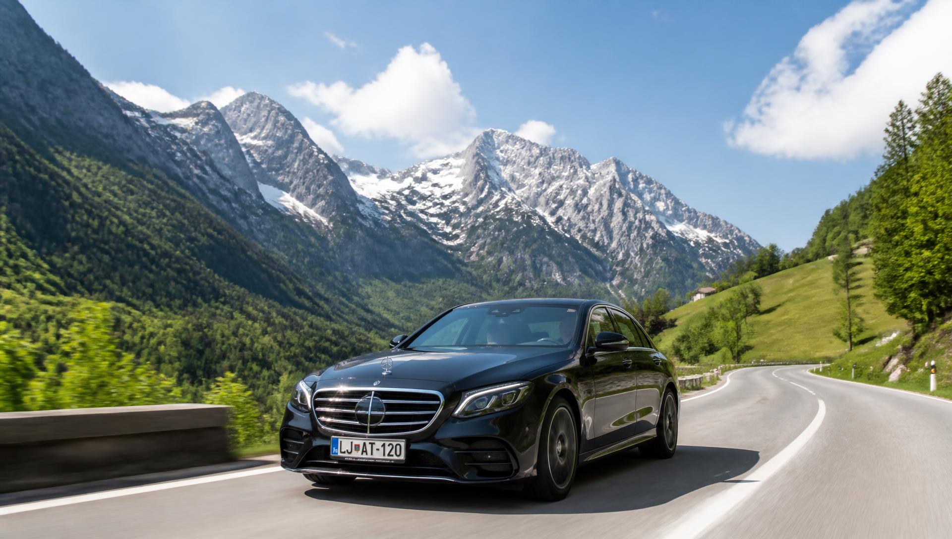 Črna limuzina Mercedes E na sončni alpski cesti, slovenske tablice